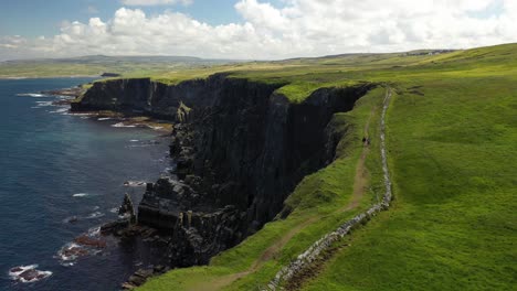 Hikers-walking-along-top-of-Cliffs-of-Moher-hiking-trail-walk,-aerial-follow