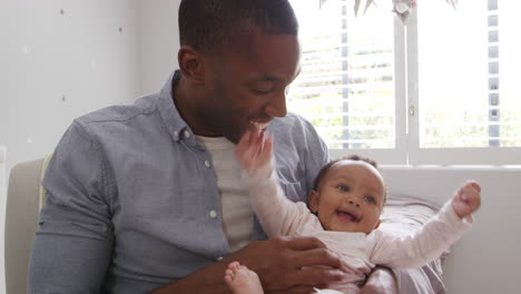 father sitting in nursery chair holding baby daughter