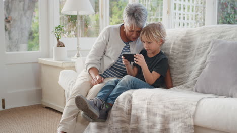 Niño-Feliz-Usando-Un-Teléfono-Inteligente-Mostrando-A-La-Abuela-Cómo-Usar-El-Teléfono-Móvil-Enseñando-A-La-Abuela-Tecnología-Moderna-Niño-Inteligente-Ayudando-A-La-Abuela-En-Casa-4k