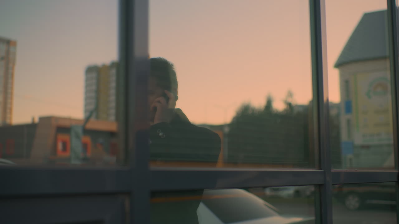 Close-up of glass reflecting red cloud and building, with someone on phone call answering in agreement, business communication, urban setting, and professional interaction
