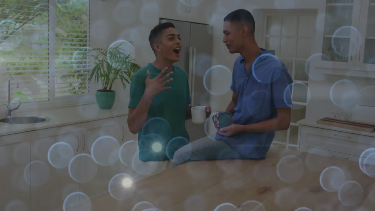 Two friends collaborating in modern kitchen, showing animated marketing charts above coffee mugs