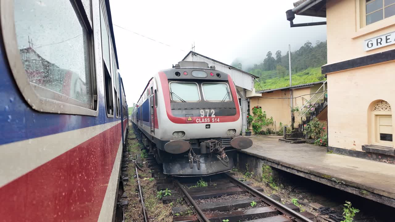 A Class S14 train passes another train at the historic Great Western station in Talawakelle, Sri Lanka, showcasing the vibrant and bustling railway system in beautiful countryside surroundings.