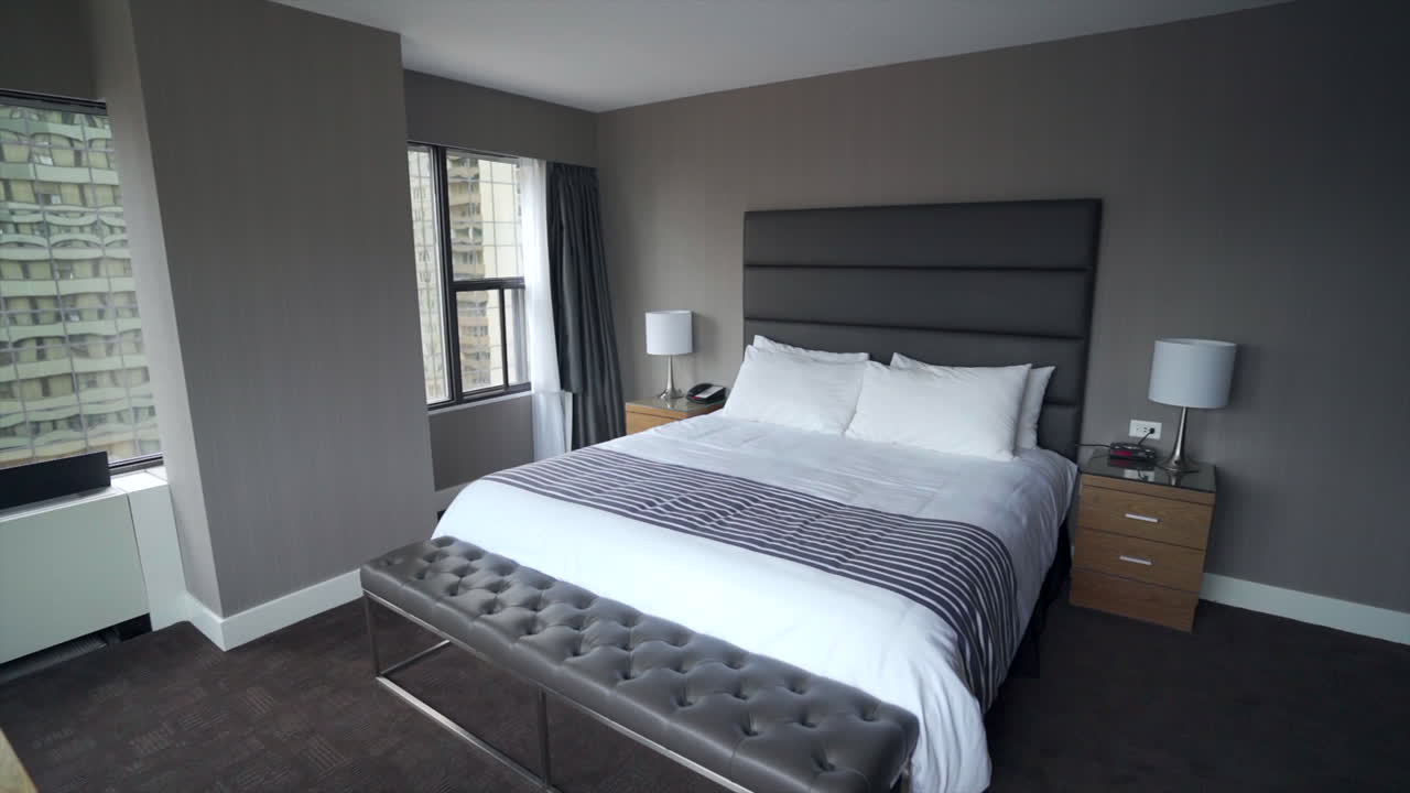 una habitación de hotel espaciosa y elegantemente diseñada con una cama tamaño king cubierta con lujosas sábanas y adornada con almohadas y una manta acogedora