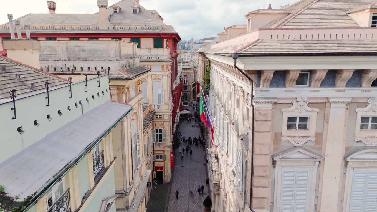 Historic street in Genoa with tall classic buildings and tourists walking through the narrow alley