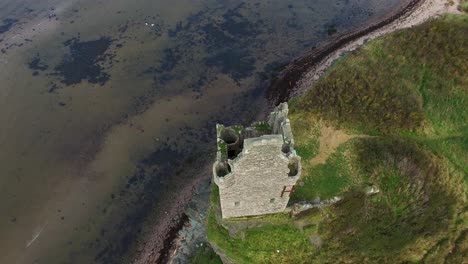 topdown ascending aerial video of a ruined stone tower on the edge of a cliff and gradually revealing the sea