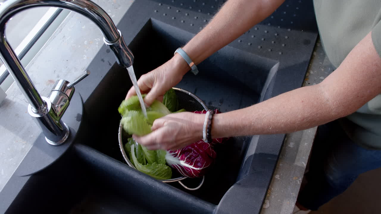 Washing fresh lettuce and radicchio, woman preparing vegetables in kitchen sink, at home
