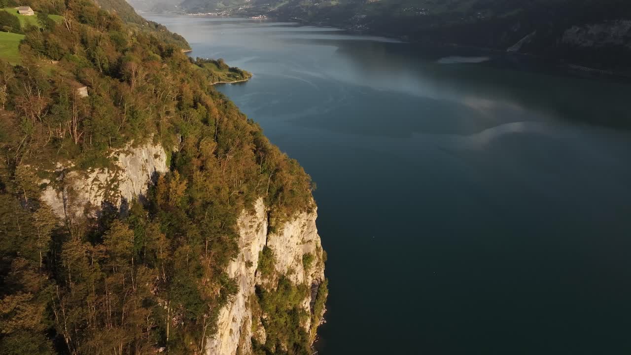 Lake Walensee in the evening during the golden hour, with autumn trees and rocky cliffs surrounding the serene water, and the town of Weesen nestled in nature. Aerial