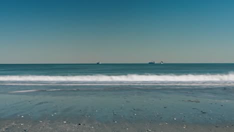 Timelapse-of-boats-on-ocean-with-waves-pushing-in-and-out-in-the-foreground