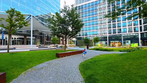child playing in modern urban park area. a child happily runs down a stone path in a sunny park, surrounded by green grass and modern buildings