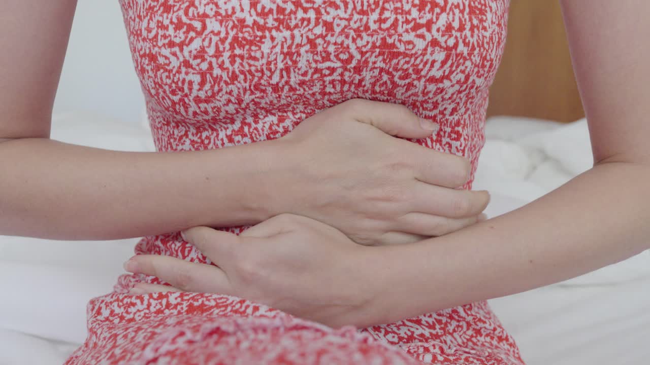 Primo piano di una donna che si stringe l'addome con entrambe le mani. Il gesto indica mal di stomaco, crampi, problemi digestivi o disagio legato a problemi di salute