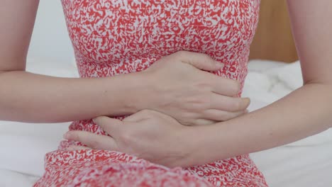 Close-up of a woman clutching her abdomen with both hands. The gesture indicates stomach ache, cramps, digestive problems, or discomfort related to health issues