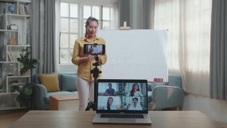 asian female teacher shoots video by smartphone camera and having video call on laptop while teaching math at home