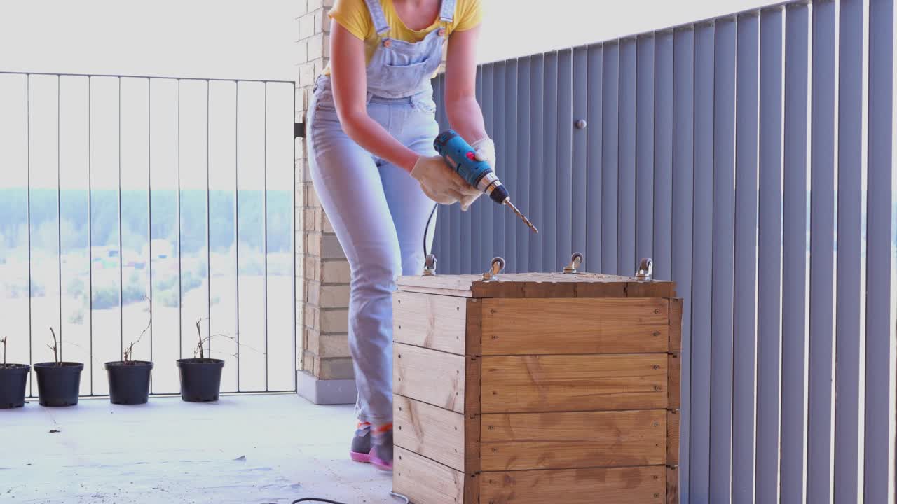 una mujer en una terraza hace un trabajo no femenino - perfora un agujero con un destornillador en una caja de madera