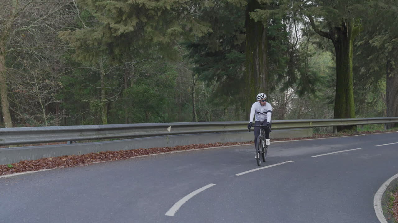 Ciclista pedalando morro acima em estrada pavimentada e vazia através da floresta.