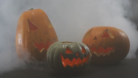 Smoke-effect-over-multiple-scary-face-carved-halloween-pumpkin-against-grey-background