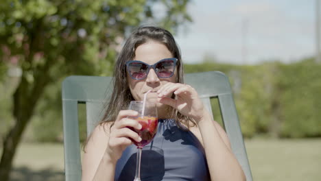 mujer feliz en bikini y gafas de sol tumbada en la tumbona, bebiendo un cóctel