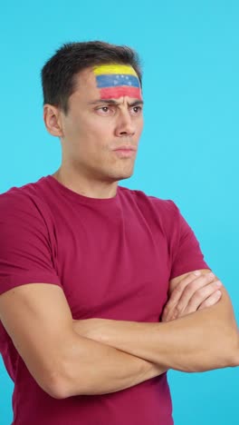 man with venezuelan flag painted looking away with serious expression