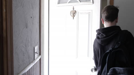 A-young-high-school-aged-teen-boy-walks-outside-of-his-house-and-closes-door