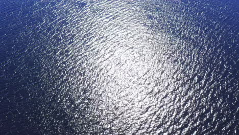 drone shot of sunlight glimmering on a wavy blue water surface