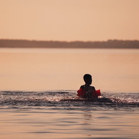 slow motion of a child in water at sunset. cute boy having fun in the river alone in the evening. silhouette of boy splashing water in the lake.