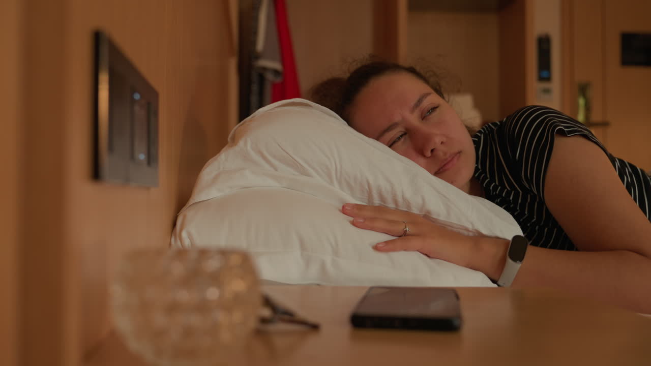 Caucasian woman asleep on hotel bedside during night, evening guest drifts to sleep reaching for smartphone, warm lamp glow, soft linens, quiet ambient mood, intimate solitude, wristwatch visible