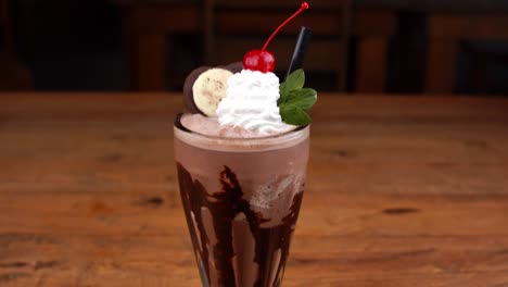 Detailed-close-up-of-chocolate-milkshake,-with-caramel,-espresso-coffee-and-whipped-cream-with-cherry,-tilt-up-and-down