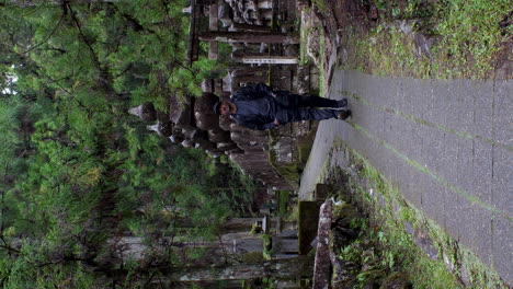 Man-in-contemplative-mood-at-Okunoin-Cemetery,-Koyasan,-among-ancient-tombstones,-vertical-shot