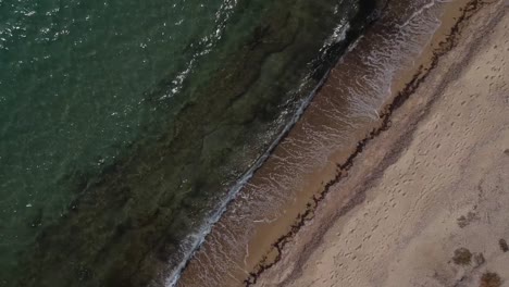 Overhead-aerial-drone-shot-over-a-golden-sandy-shore-and-the-blue-sea-of-Mediterranean-sea-close-to-Thessaloniki,-Greece-in-Epanomi