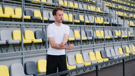 junger männlicher athlet der fitness, der arme im stadion ausdehnt