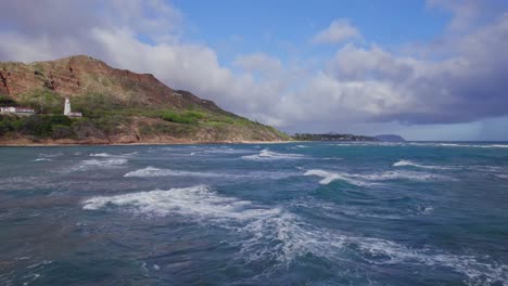 Imágenes-De-Drones-De-Aguas-Turquesas-Cubiertas-De-Blanco-Del-Océano-Pacífico-Conducen-Al-Faro-De-Diamond-Head-Con-La-Formación-Volcánica-De-Diamond-Head-En-El-Horizonte-Contra-El-Cielo-Azul