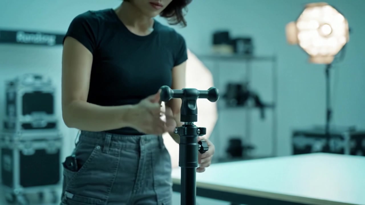 Setting Up a Studio Lighting Stand: Step-by-Step Assembly by a Female Photographer in a Creative Workspace with Bright Backgrounds and Equipment Visible