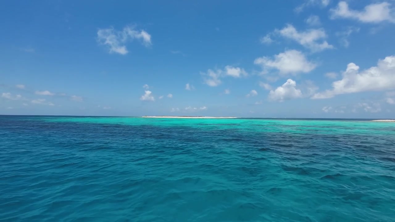 Kristallklares türkisfarbenes Wasser der Karibik erstreckt sich unter blauem Himmel bis zu einer fernen Sandinsel