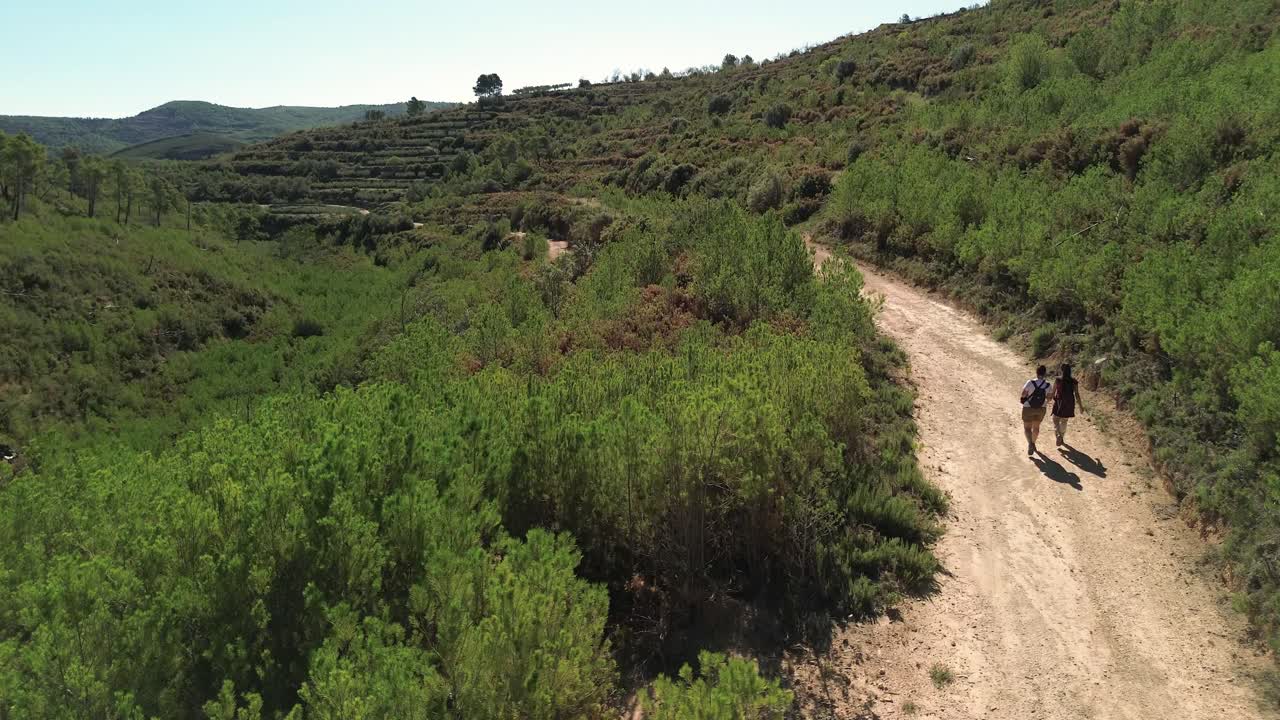seguimiento disparo de drone de dos chicas morenas caminando en un día soleado a lo largo de un camino rodeado de vegetación