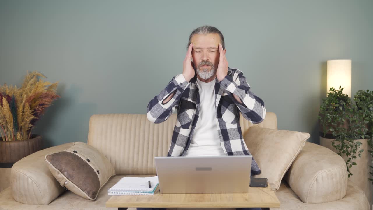 노트북으로 일하는 남자가 두통을  ⁇ 고 있습니다.
