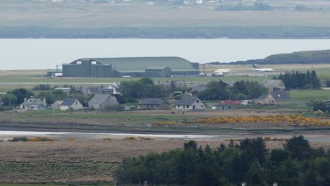 shot of an airport, plane, runway and airplane hangar in the distance beyond the small, seaside town of stornoway