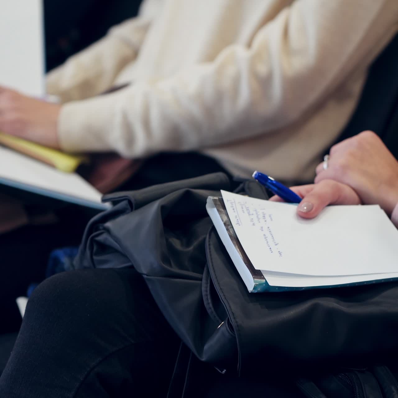 Women sitting in a row during the conference. Young females hold copybooks and write important information during the seminar. Close-up.