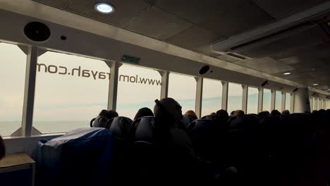silhouetted passengers seated inside a speedboat ferry during a daytime journey. natural light illuminates through large windows, creating a serene travel atmosphere on the water.