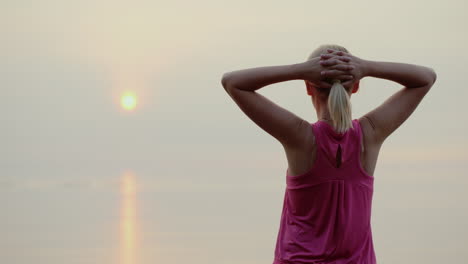 confident fitness woman looking at dawn over the sea rear view