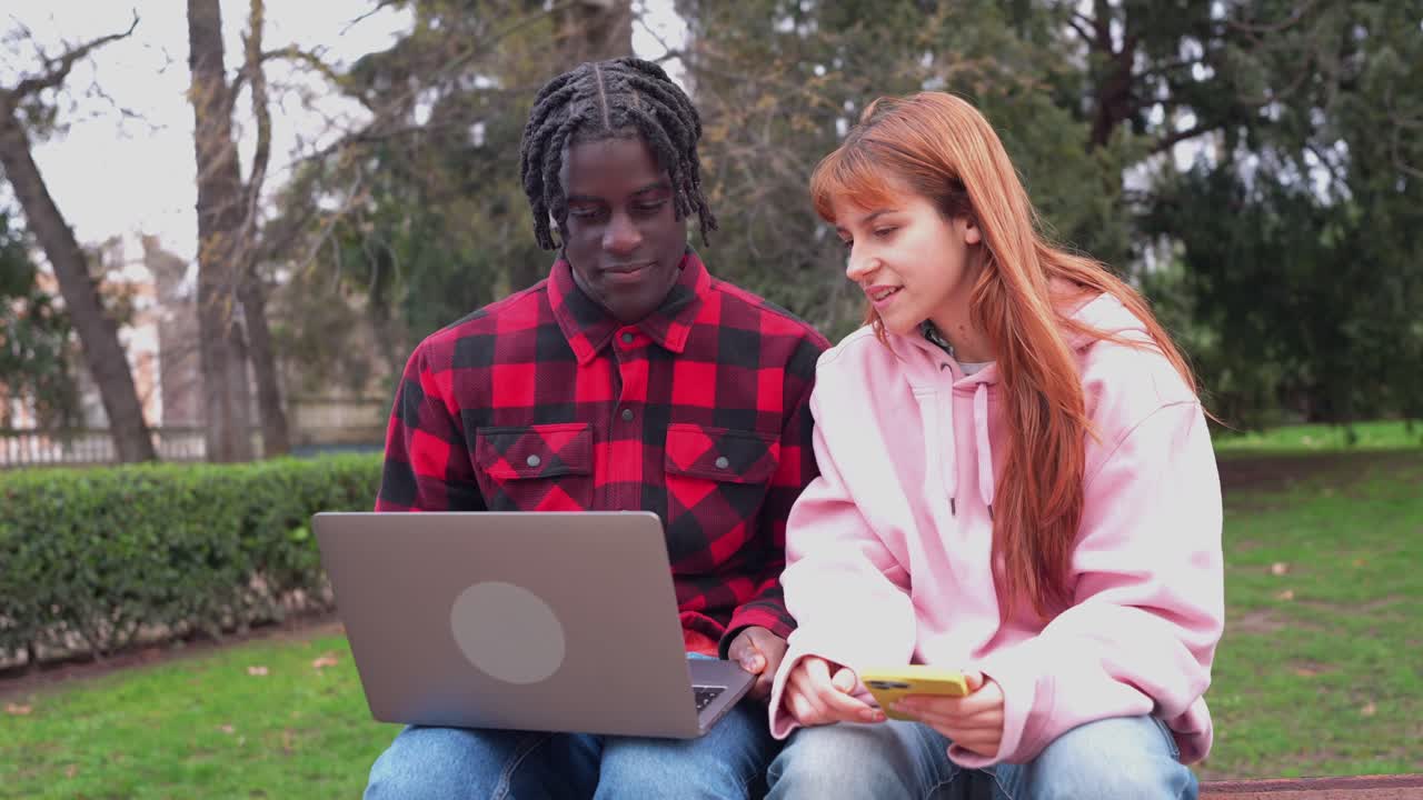 Duas pessoas usando um laptop e um celular em um parque