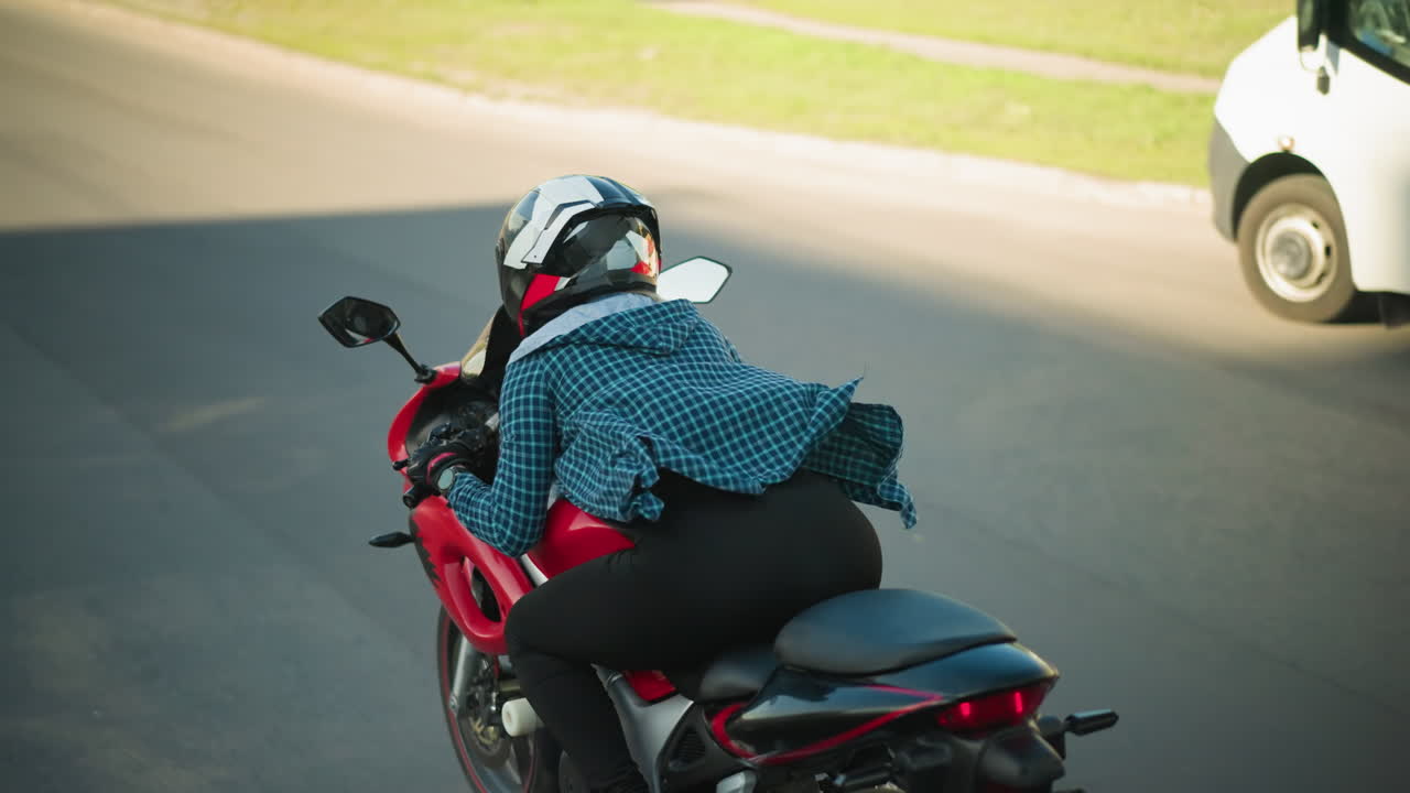 한 여성 오토바이 운전자가 빨간색 파워바이크를 타고 앞으로 기울어서 도시 도로에서 파란색 버스와 색 차를 뛰어넘으며, 그녀의 체크 된 셔츠가 바람에 날아갑니다.