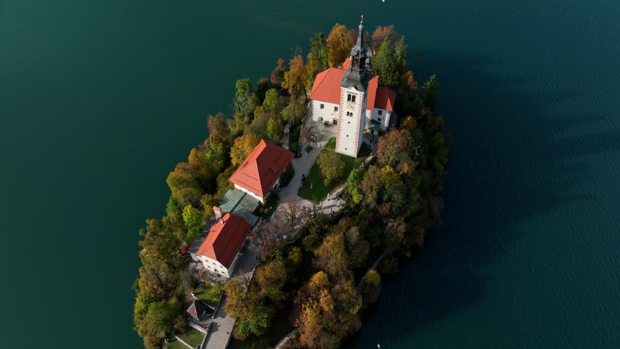 Luftfoto i stigende bane rundt Bled slott på en klippe over Bledsjøen, omgitt av skog og blått vann
