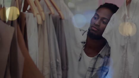 animation of bokeh lights over african american man tidying clothes display in shop
