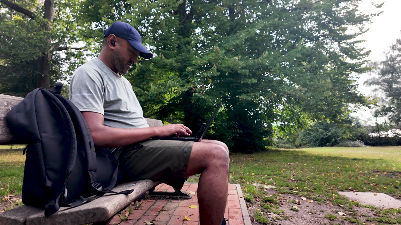 Man using laptop while sitting on a park bench, enjoying remote work outdoors