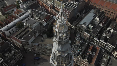 Vista-Aérea-Del-Campanario-De-La-Antigua-Iglesia-Con-Un-Reloj-Con-Edificios-Y-Apartamentos-Al-Fondo-Durante-El-Día-En-Amsterdam,-Países-Bajos