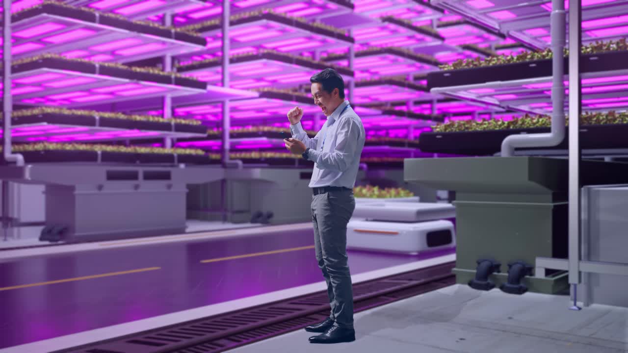 vista lateral completa del cuerpo de un trabajador profesional masculino asiático de pie con su teléfono en una granja vertical, instalación industrial de alta tecnología, levanta el puño con el objetivo de gritar