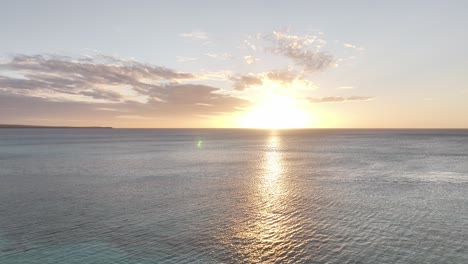 Órbita-Aérea-Alrededor-Del-Atardecer-Mientras-La-Luz-Se-Esconde-Bajo-El-Horizonte-Con-El-Haz-Sobre-El-Agua-Brillante