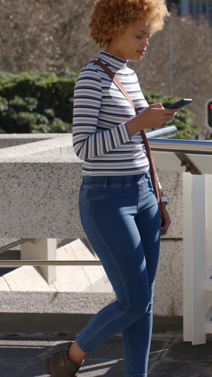 Video verticale: Donna che supera un parapetto di cemento mentre tocca lo smartphone su una passerella sopraelevata.