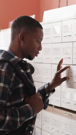 student closes drawer opening another box. young dark-skinned man disappointed by absence of necessary card in drawer. searching in paper storage