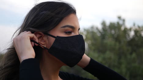 Attractive-hispanic-woman-putting-on-a-reusable-cloth-respiratory-face-mask-to-prevent-infection-from-the-corona-virus-while-social-distancing-in-quarantine-during-the-pandemic