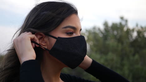 attractive hispanic woman putting on a reusable cloth respiratory face mask to prevent infection from the corona virus while social distancing in quarantine during the pandemic